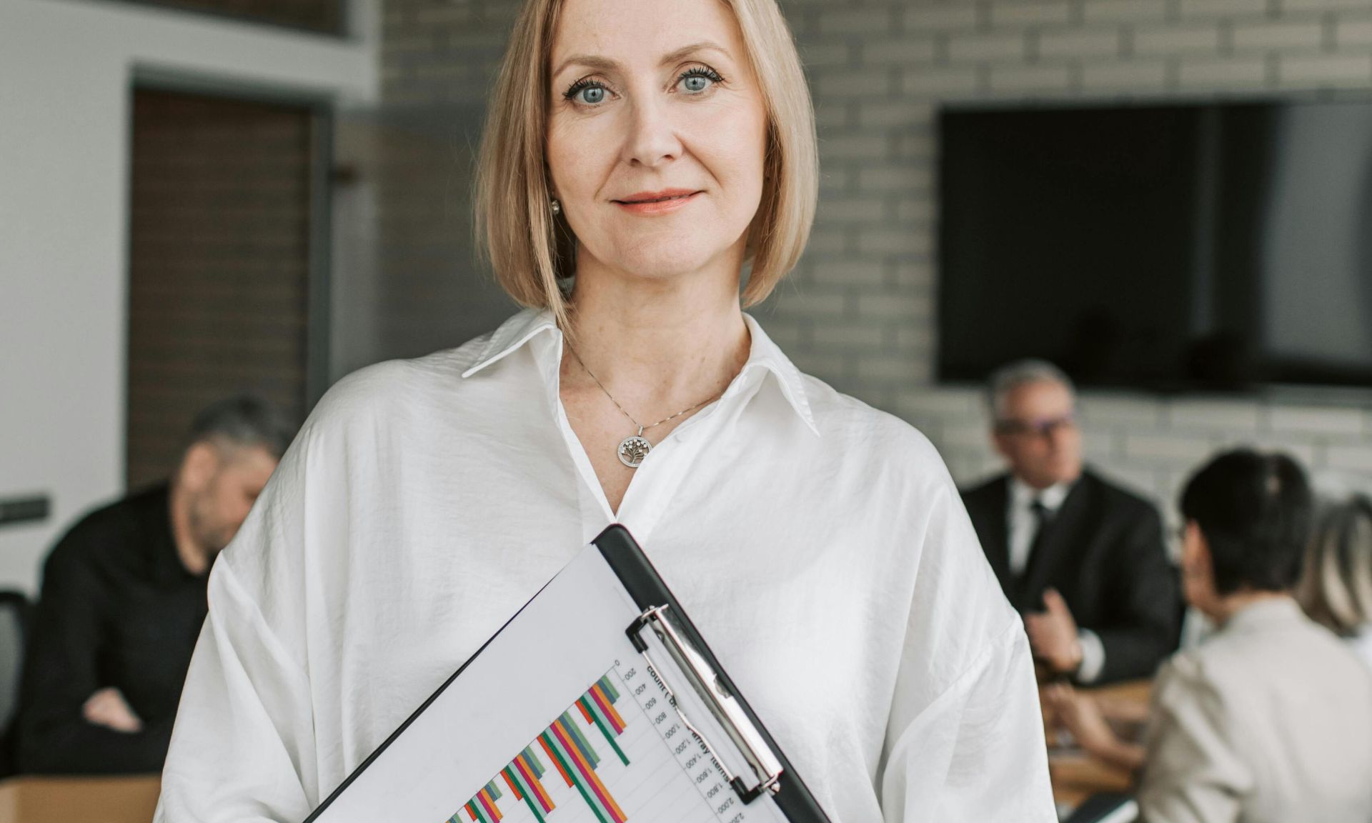 Professional woman holding clipboard in corporate office setting during a business meeting.